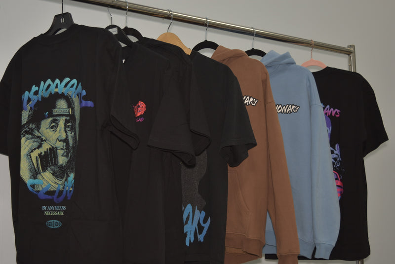 Collection of hoodies and t-shirts hanging on a rack against a plain wall.