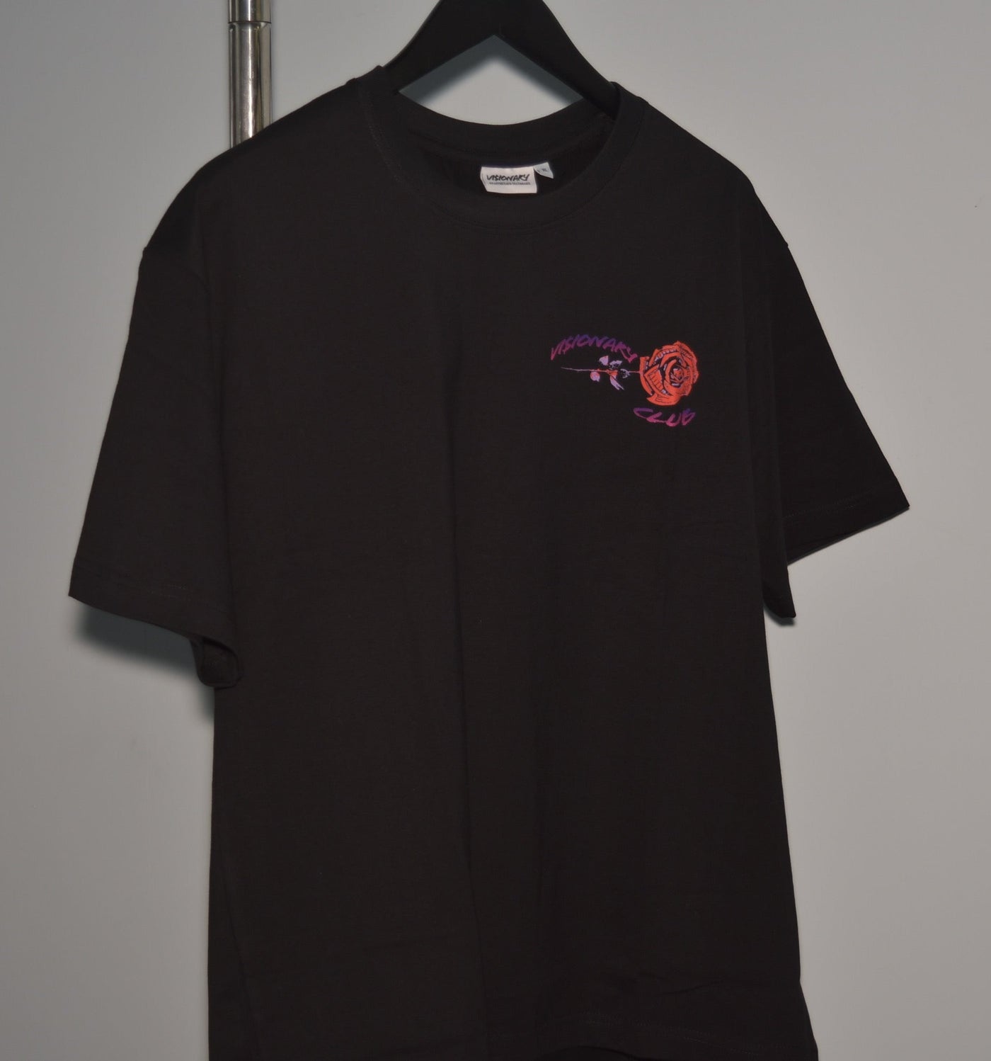 Black t-shirt with a small logo on a hanger against a gray background