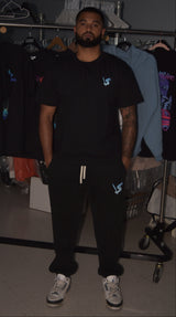 Man wearing a black t-shirt and pants with logos in a clothing store.